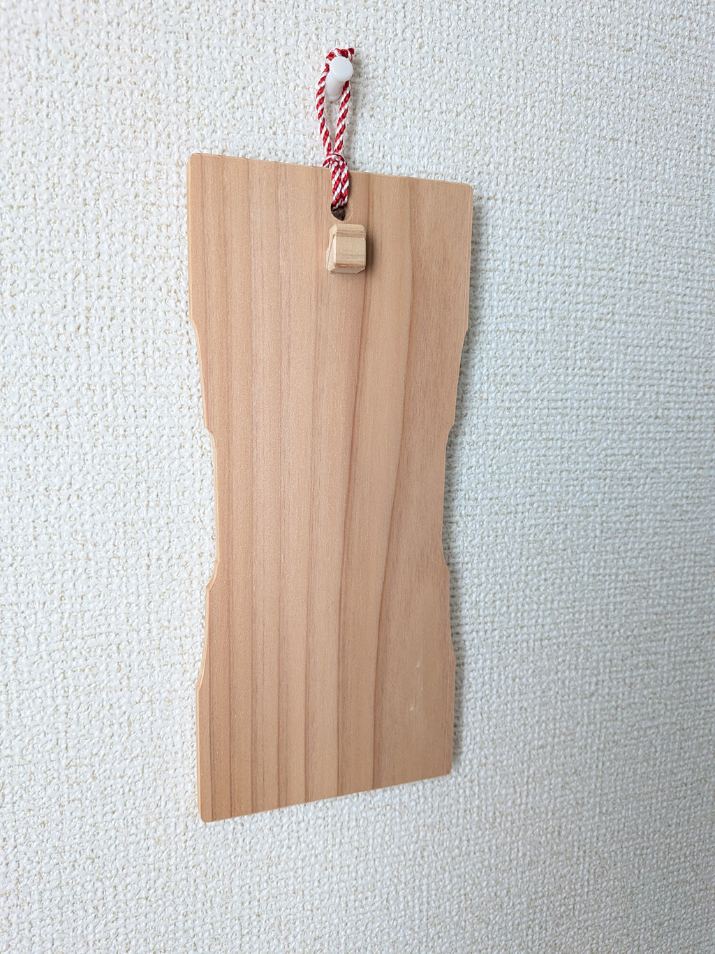 お守りを掛けていないinori 壁掛けver.を斜めから見たところ。紅白の紐で画鋲に掛けている