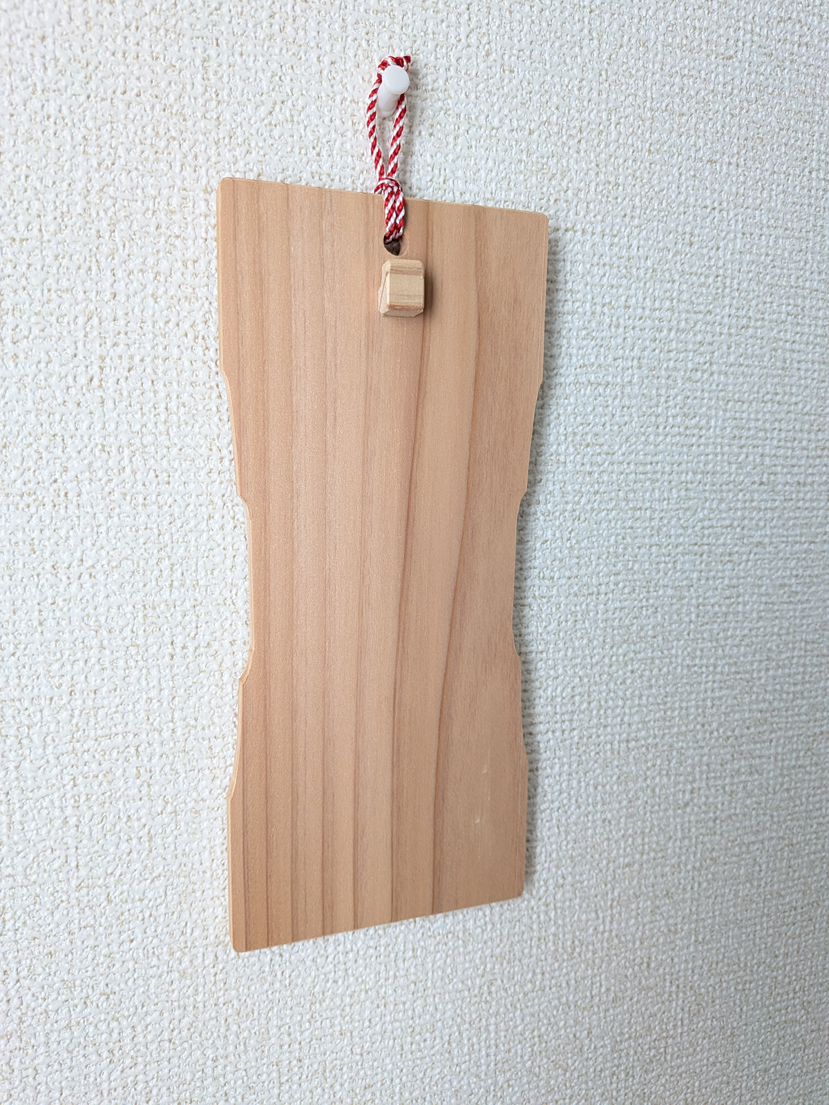 お守りを掛けていないinori 壁掛けver.を斜めから見たところ。紅白の紐で画鋲に掛けている