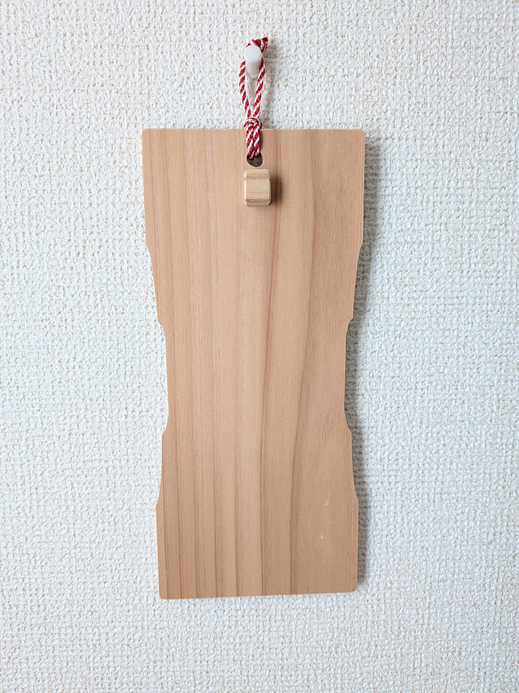 inori 壁掛けver.を壁に掛け、正面から見たところ。中ほどがくびれた杉の板で、上部に紅白の紐と小さな木の突起がついている