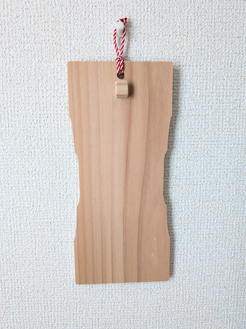 inori 壁掛けver.を壁に掛け、正面から見たところ。中ほどがくびれた杉の板で、上部に紅白の紐と小さな木の突起がついている